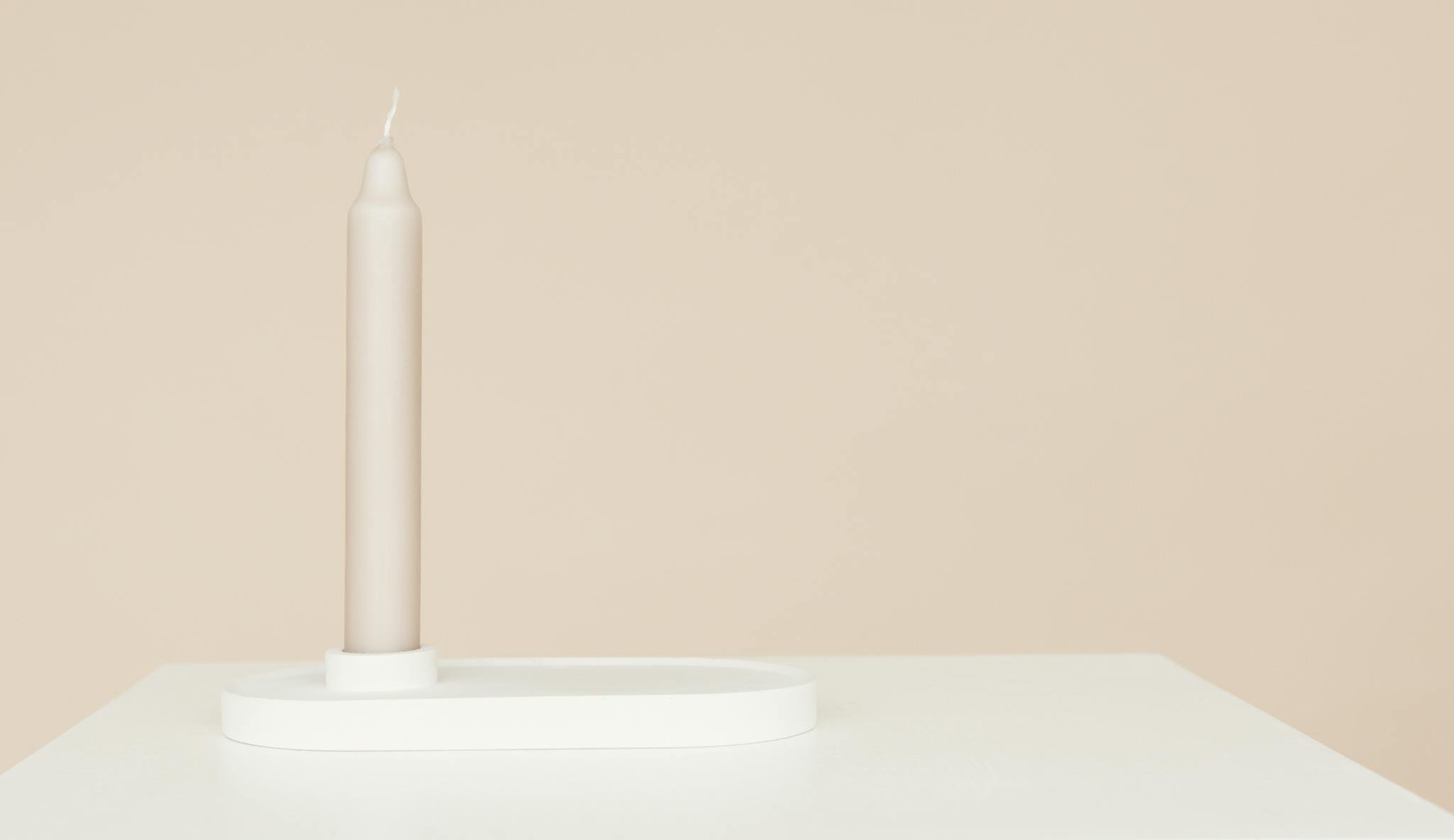 A single beige candle on a white table with a soft neutral background.