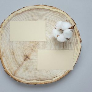 Top view of two blank business cards on a round wooden coaster with cotton, perfect for design mockups and presentations.